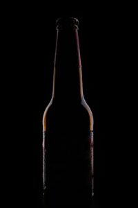 A glass of dark beer beside a glass of light beer on a wooden table, both in natural daylight.