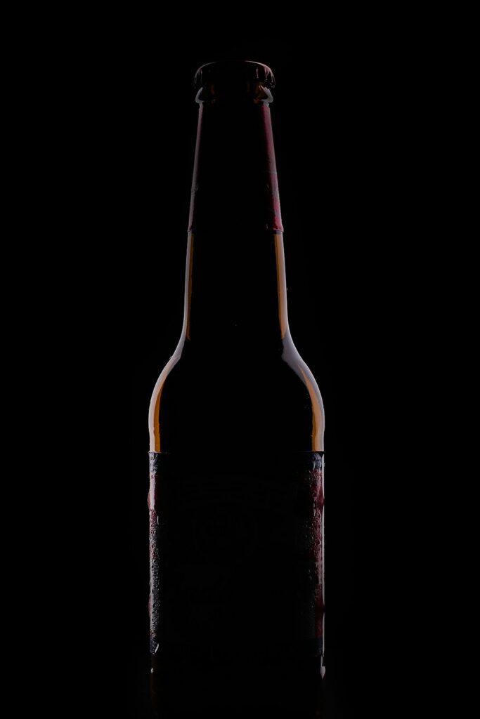 A glass of dark beer beside a glass of light beer on a wooden table, both in natural daylight.