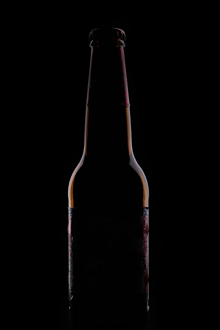 A glass of dark beer beside a glass of light beer on a wooden table, both in natural daylight.