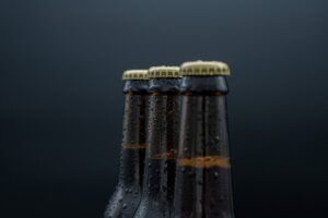 A person places bottled beer into a shaded cooler during a sunny outdoor gathering.