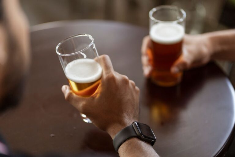 People at a backyard table enjoying glasses of assorted beers in different colors and styles.