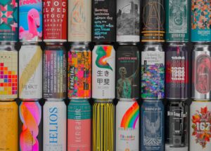 A person examines a beer can showing style, alcohol content, ingredients, and date markings.
