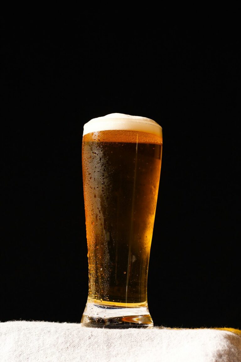 A person pours golden beer into a tilted tulip glass beside several clean glass styles.